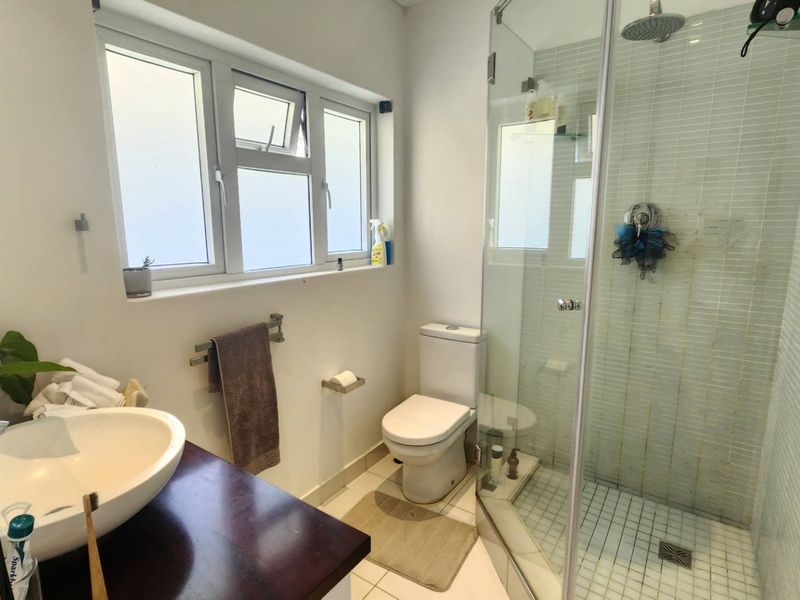 A functional bathroom featuring a vessel sink on a dark vanity, a toilet, and a glass-enclosed shower with tiled finishes and a rain shower head.