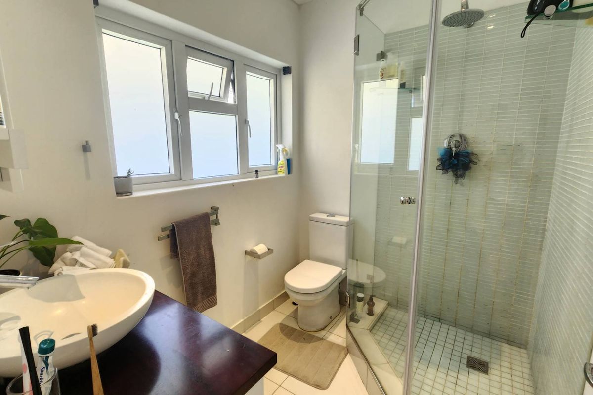 A functional bathroom featuring a vessel sink on a dark vanity, a toilet, and a glass-enclosed shower with tiled finishes and a rain shower head.