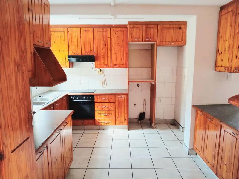 A functional kitchen featuring wooden cabinetry, built-in oven, electric hob, extractor fan, and tiled flooring with dedicated space for appliances.