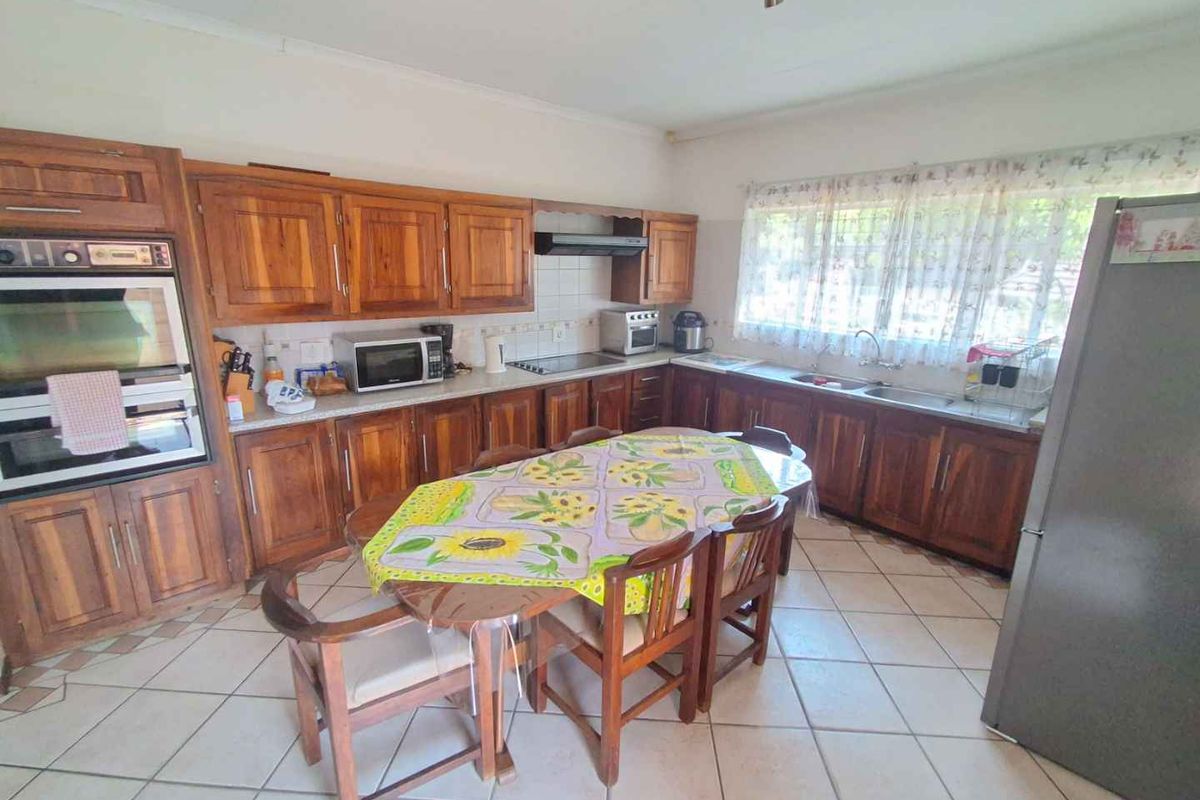 Spacious kitchen featuring extensive wooden cabinetry, built-in oven, extractor fan, double sink, and tiled flooring, offering a functional layout with ample storage space.