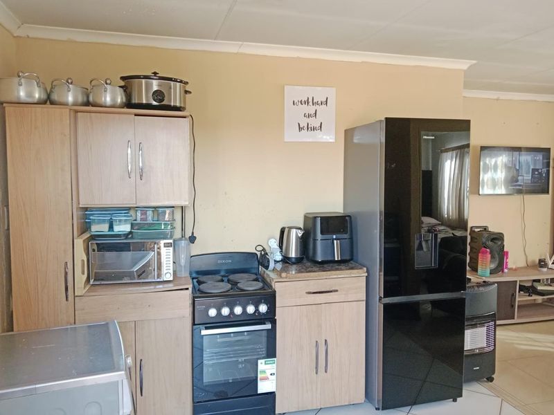 A functional kitchen area featuring light wood-finish cabinetry, a freestanding stove with oven, and tiled flooring, providing essential cooking and storage space.