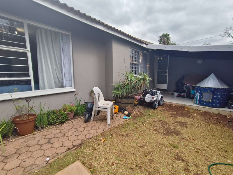 Rear exterior view of the townhouse featuring a paved walkway, a small covered patio area, and a garden space with established lawn.