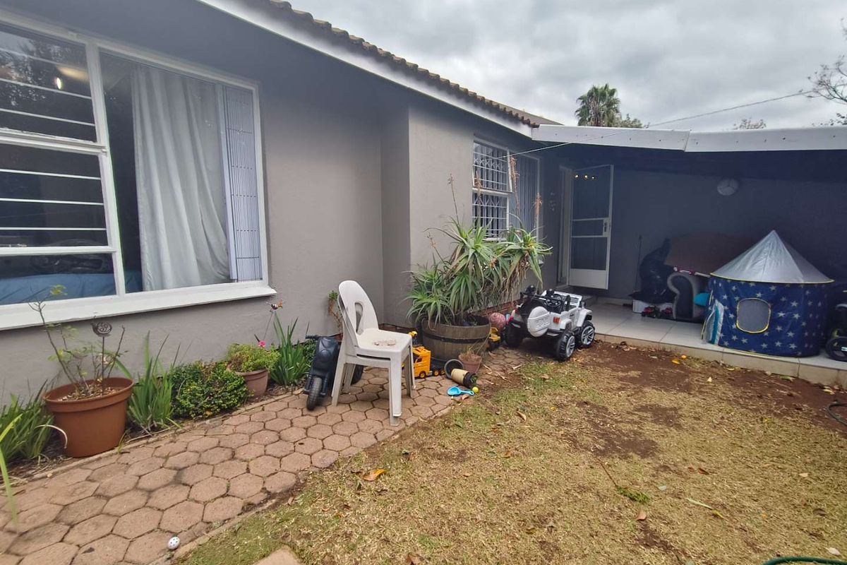 Rear exterior view of the townhouse featuring a paved walkway, a small covered patio area, and a garden space with established lawn.