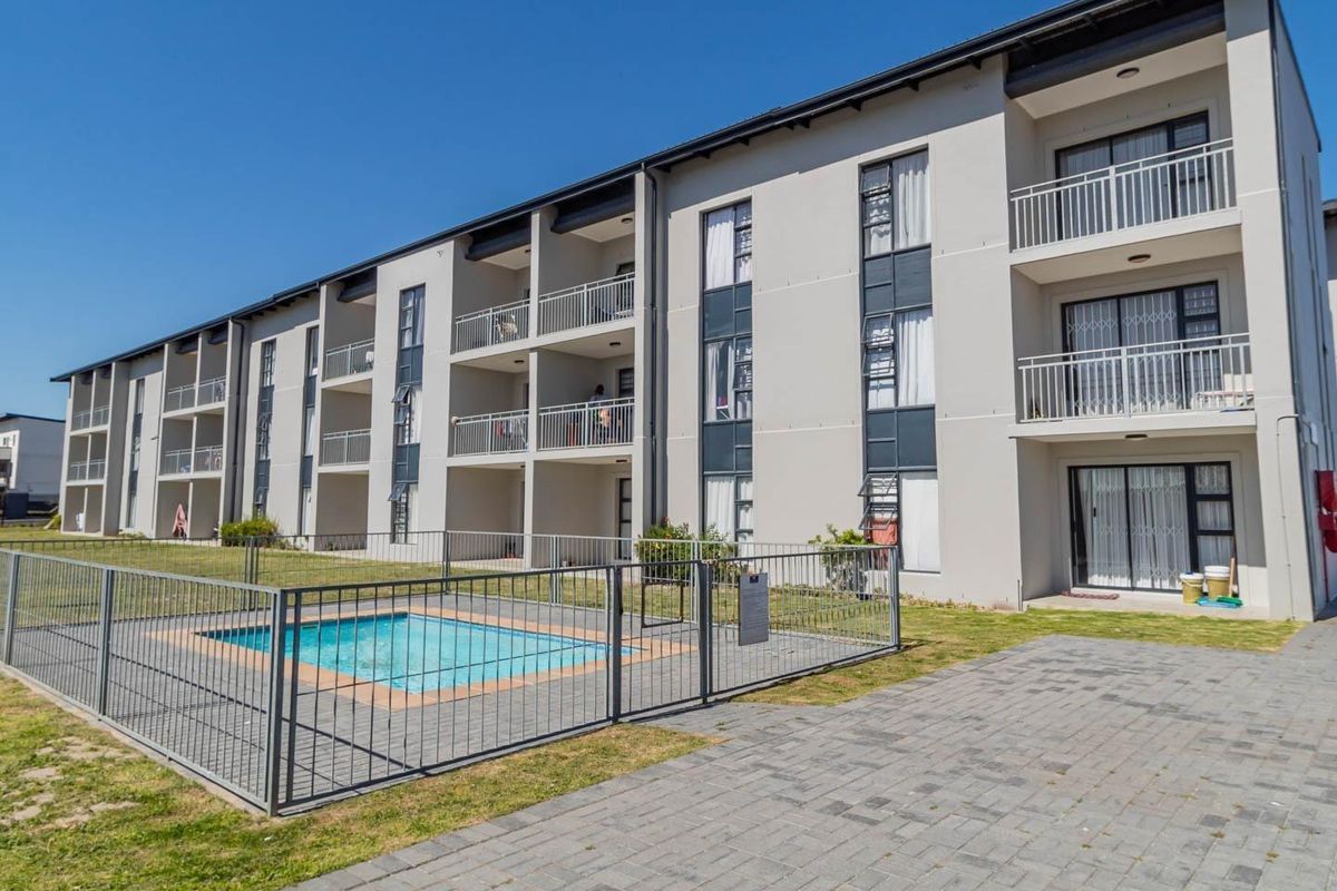 Exterior view of a modern apartment complex featuring a communal swimming pool, paved walkways, and private balconies for each unit.