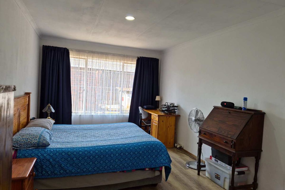 A functional bedroom featuring laminate flooring, recessed ceiling lighting, and large windows with curtain rails, offering a neutral base for personalization.