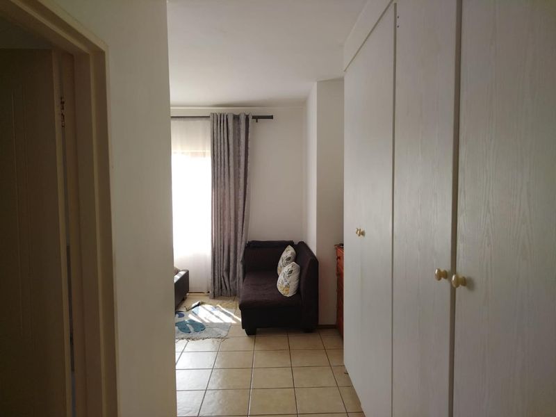 A functional hallway featuring tiled flooring and ample built-in cupboard storage, leading towards a bright living area.