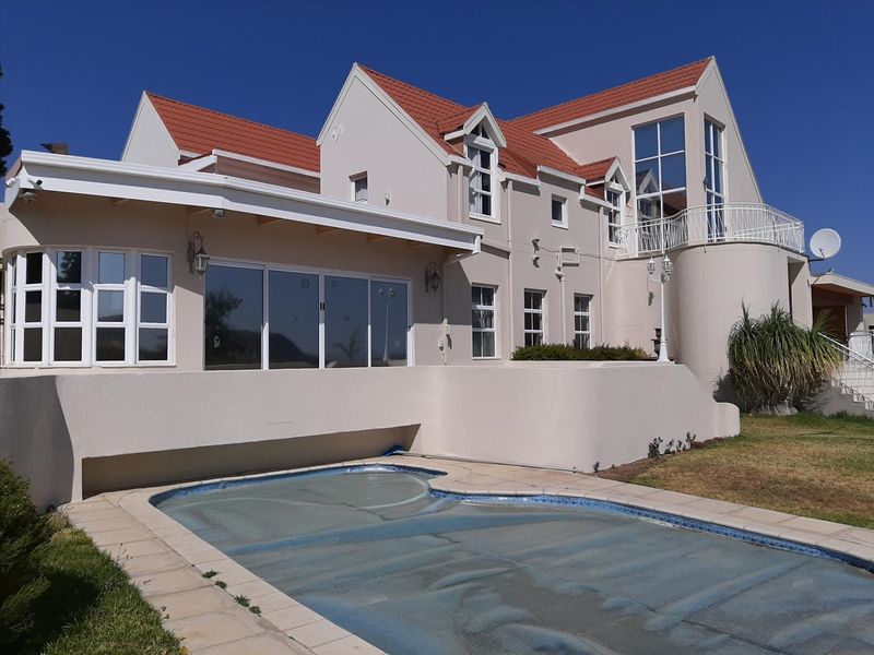 Rear view of a multi-story residential property featuring a swimming pool with cover, a balcony, and large sliding glass doors leading to the interior.