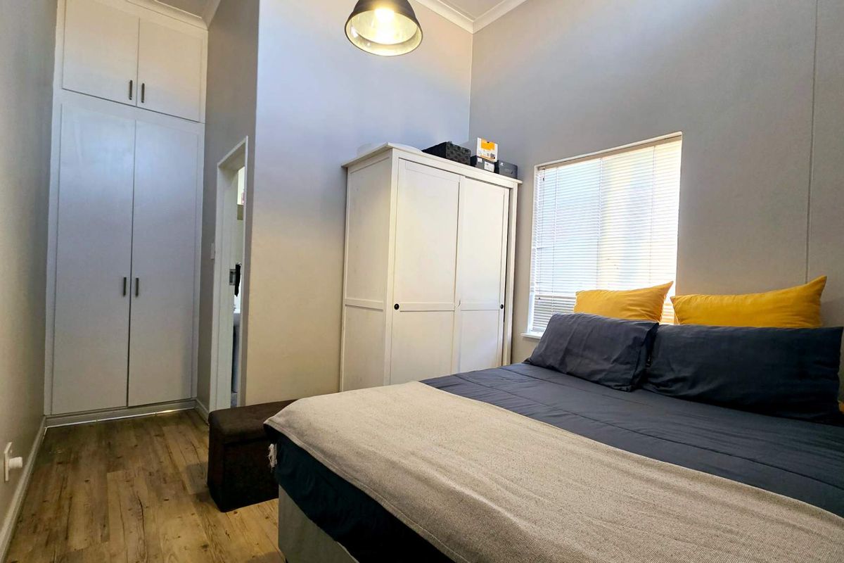 A well-lit bedroom featuring built-in floor-to-ceiling cabinetry, wood-look flooring, and a window with fitted blinds.