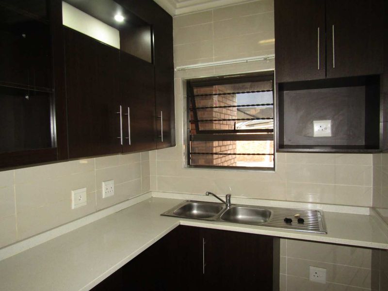 A functional kitchen featuring dark wood cabinetry, stone countertops, a stainless steel double sink, and tiled backsplash with integrated electrical outlets.
