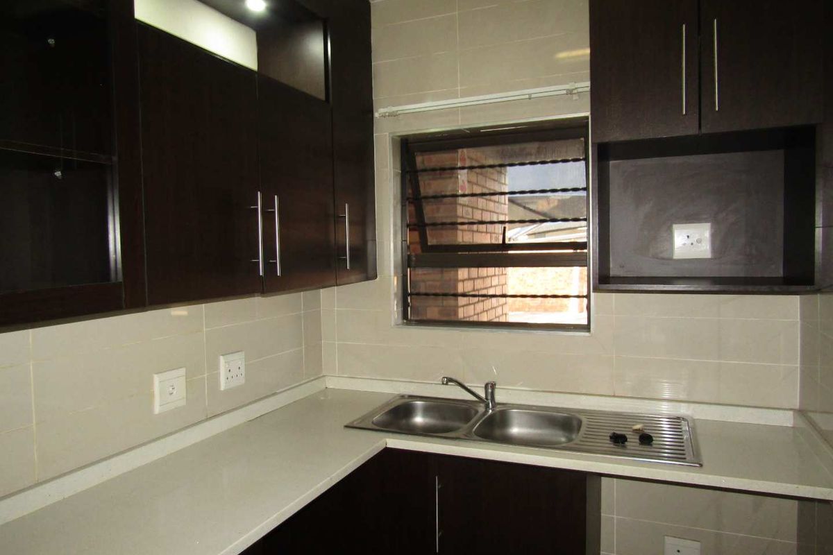 A functional kitchen featuring dark wood cabinetry, stone countertops, a stainless steel double sink, and tiled backsplash with integrated electrical outlets.
