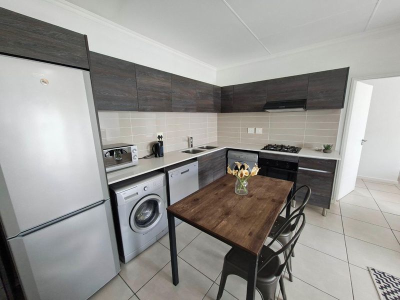 Modern kitchen featuring dark wood-finish cabinetry, gas hob, extractor fan, under-counter oven, and tiled flooring with a functional layout.