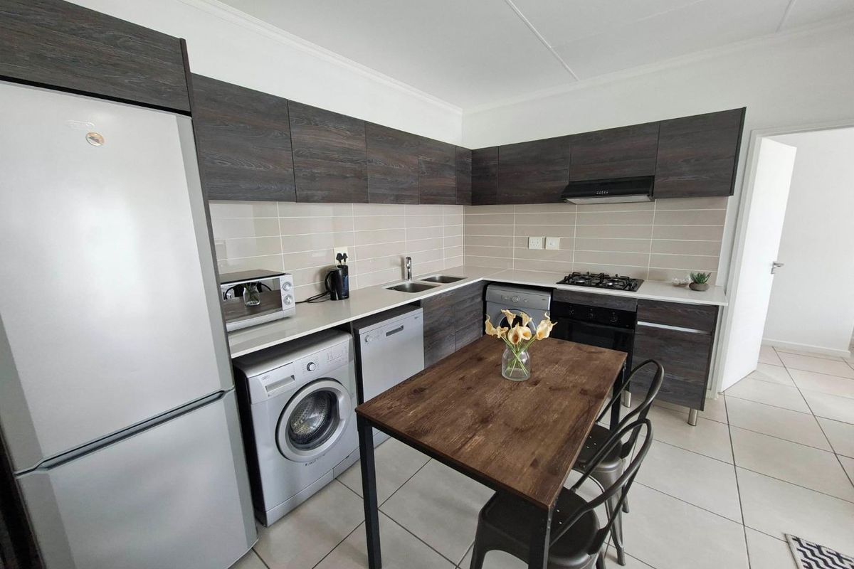 Modern kitchen featuring dark wood-finish cabinetry, gas hob, extractor fan, under-counter oven, and tiled flooring with a functional layout.