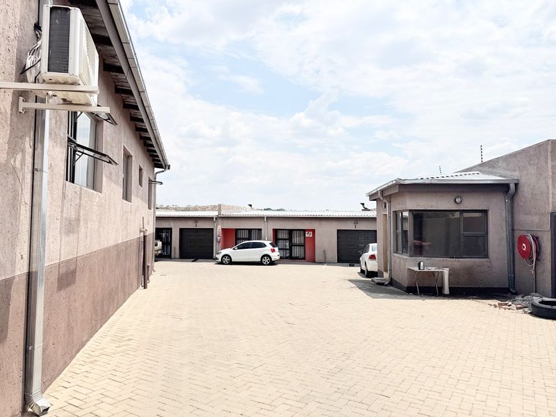 A paved driveway area leading to multiple garage units, featuring exterior wall-mounted air conditioning and security infrastructure.