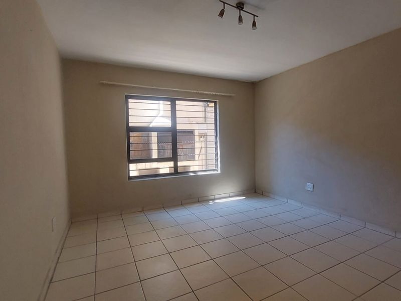 An empty bedroom featuring tiled flooring, security bars on the window, and a ceiling-mounted light fixture, ready for personalization.