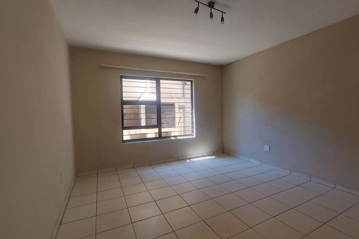An empty bedroom featuring tiled flooring, security bars on the window, and a ceiling-mounted light fixture, ready for personalization.
