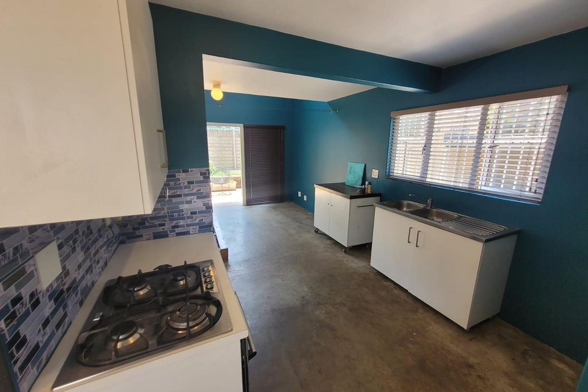 Open-plan kitchen area featuring a gas hob, stainless steel sink, tiled splashback, and built-in cabinetry with direct access to an outdoor patio space.