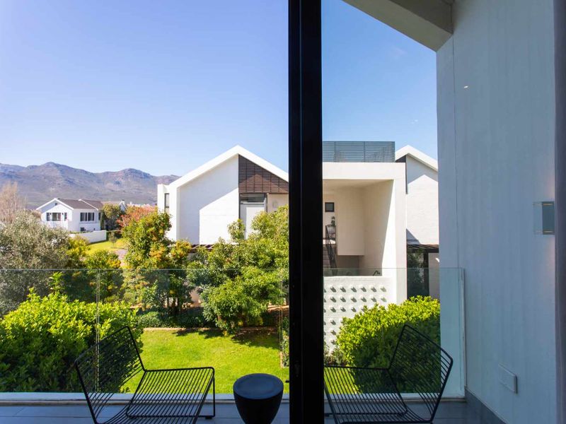 A modern balcony featuring a sleek glass balustrade and tiled flooring, offering a pleasant view of the surrounding garden and mountain landscape.