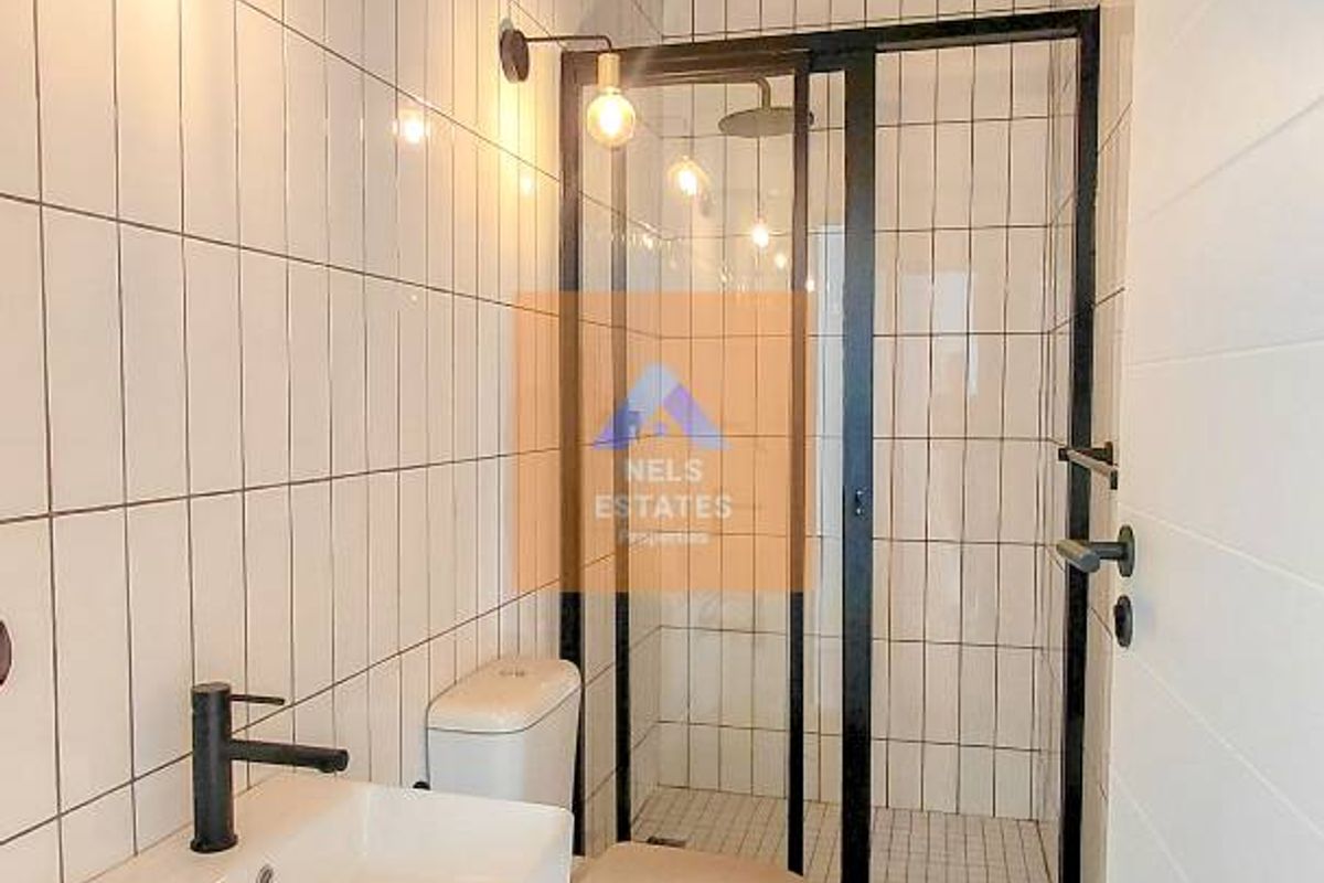 Modern bathroom featuring a wall-mounted basin, black fixtures, a glass-enclosed shower, and a distinctive timber-paneled ceiling.