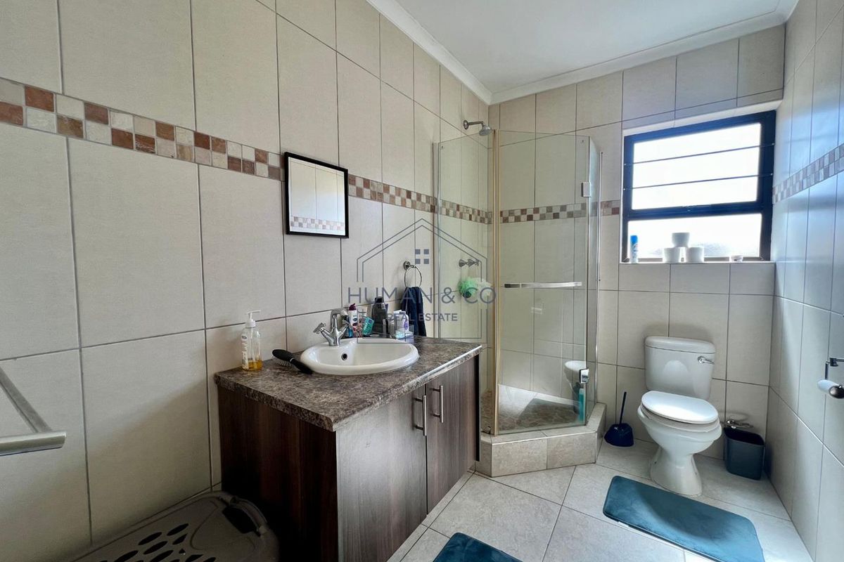 A functional bathroom featuring a corner glass shower enclosure, a vanity with a basin, and a standard toilet, finished with neutral wall and floor tiles.