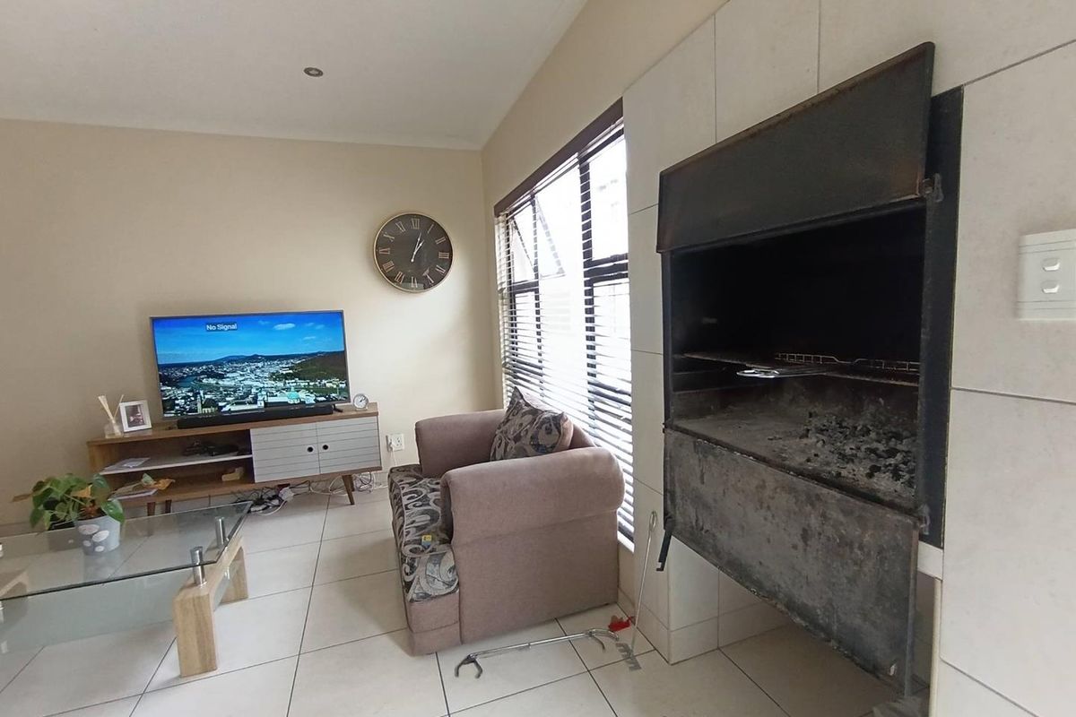 Living area featuring a built-in indoor braai fireplace, tiled flooring, and large windows with fitted blinds.