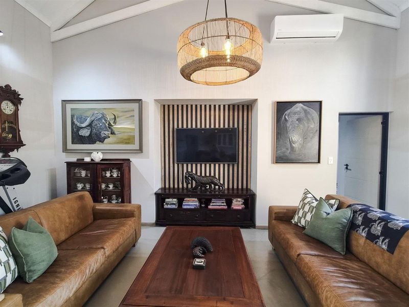 A well-maintained living room featuring a vaulted ceiling with exposed beams, a slatted timber feature wall with a media niche, and air conditioning.