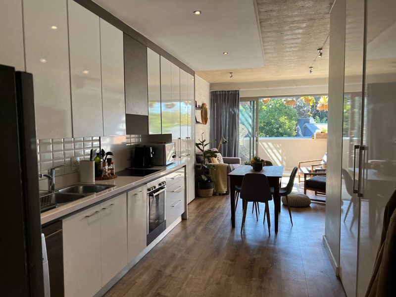 Modern open-plan kitchen and dining area featuring sleek cabinetry, integrated appliances, and direct access to a private balcony through sliding glass doors.