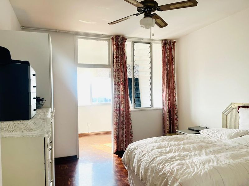A bedroom featuring parquet flooring, a ceiling fan, and louver windows with direct access to an adjoining balcony area.
