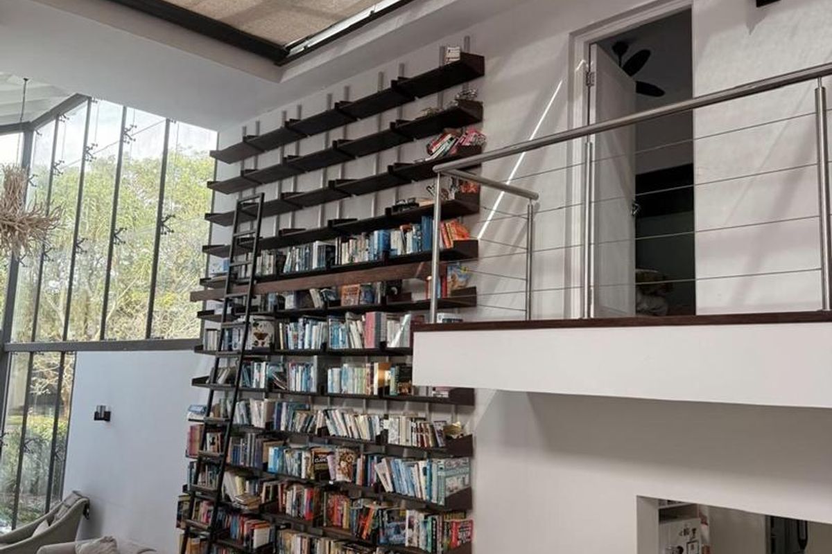 Spacious double-volume living area featuring a dramatic floor-to-ceiling library wall with sliding ladder, mezzanine level, and expansive skylight for natural light.