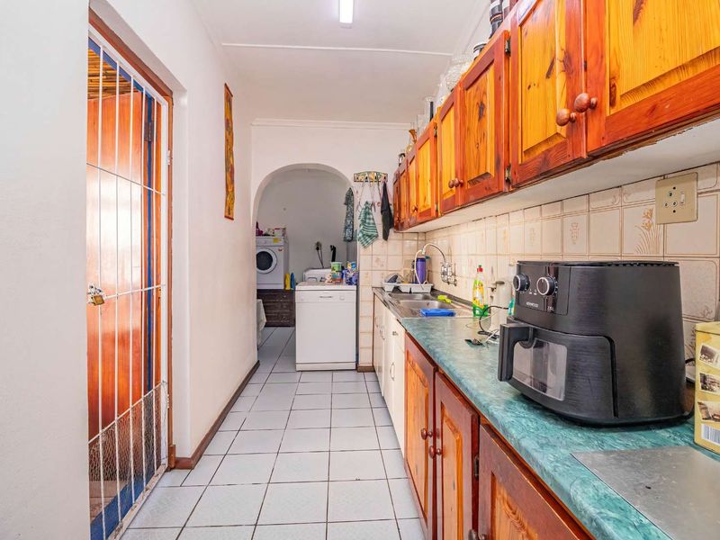 A functional kitchen featuring wooden cabinetry, tiled backsplash, and laminate countertops, with an adjacent laundry area visible through an arched doorway.
