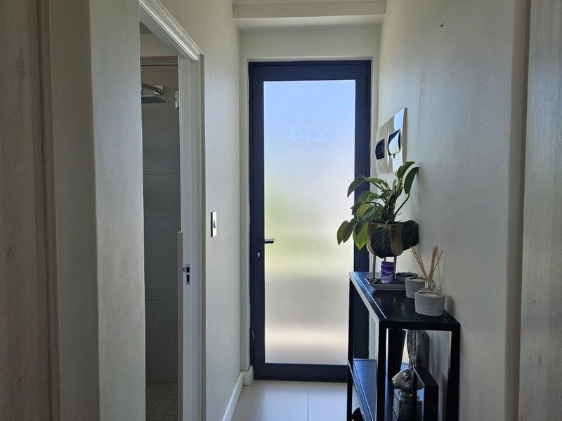 A bright hallway featuring tiled flooring, recessed ceiling lighting, and a modern frosted glass exterior door leading to the outside.