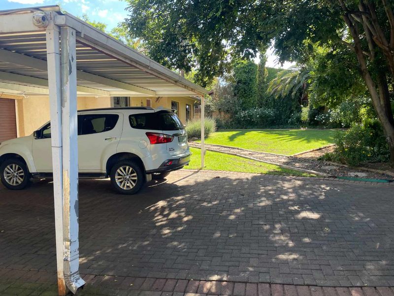 A paved driveway featuring a covered carport and a well-maintained garden area.