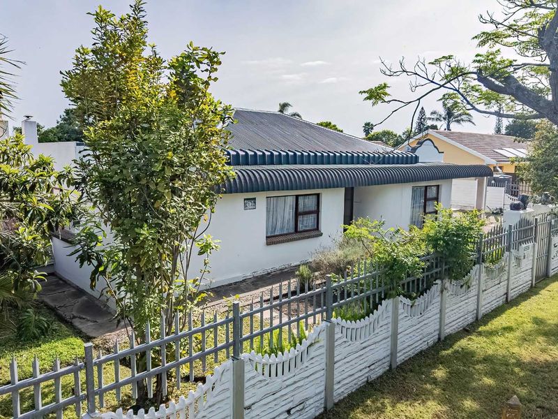 Front elevation of a single-story house featuring a corrugated metal roof, white exterior walls, and a secure perimeter boundary wall with metal fencing.