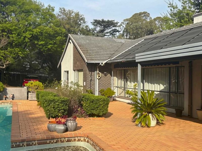 Rear exterior view featuring a brick-paved patio area, a swimming pool, and a well-maintained garden setting with a tiled roof structure.