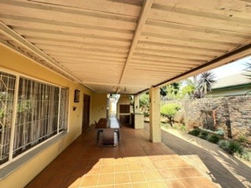 A covered outdoor patio featuring tiled flooring and a built-in braai area, overlooking a private garden with a brick boundary wall.