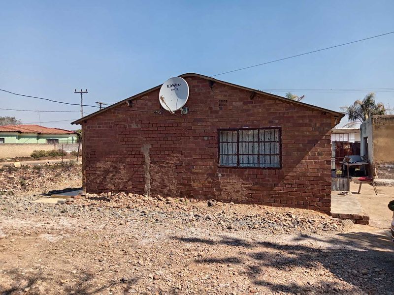 Rear view of a single-story exposed brick house featuring a window with security bars and a satellite dish mounted on the gable wall.