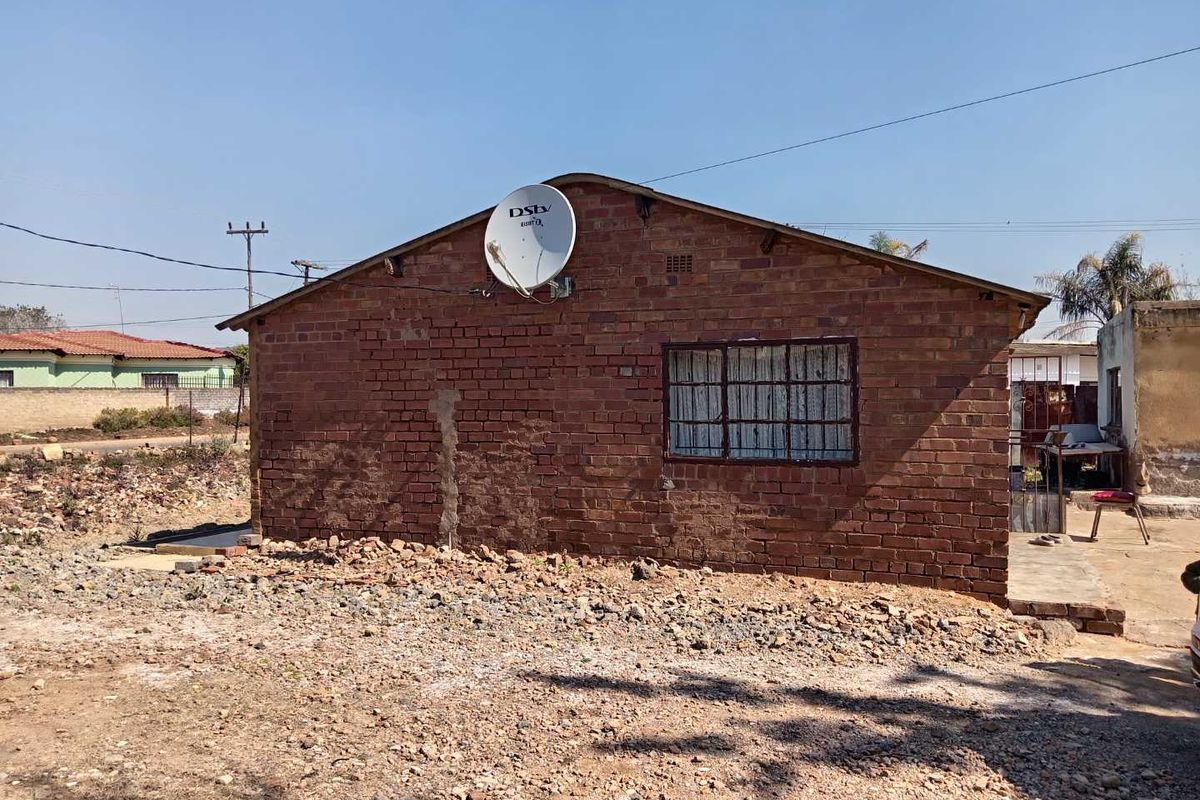 Rear view of a single-story exposed brick house featuring a window with security bars and a satellite dish mounted on the gable wall.