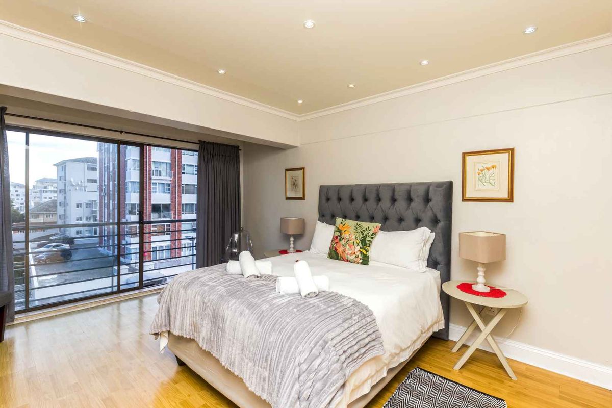 A well-maintained bedroom featuring hardwood flooring, recessed downlighting, crown molding, and a large sliding glass door providing access to the balcony.