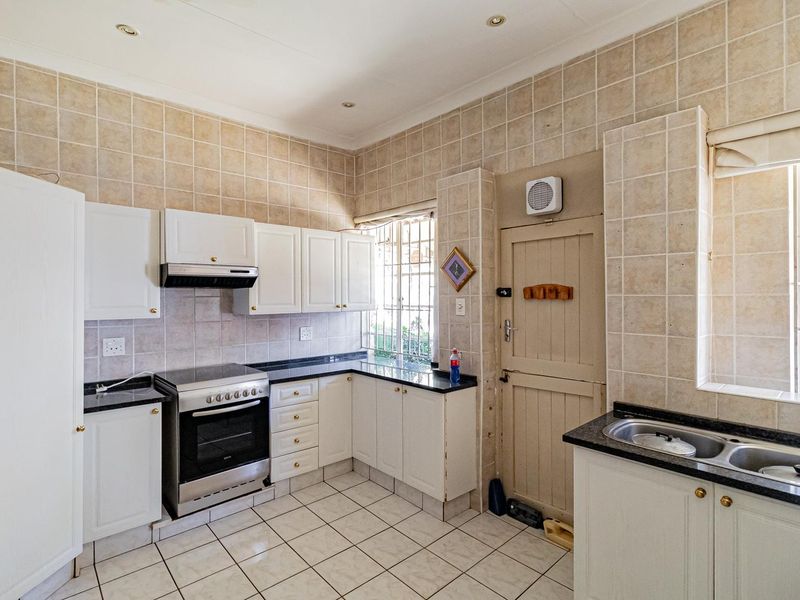 A functional kitchen featuring white cabinetry, granite countertops, a double bowl sink, and a freestanding stove with an extractor fan.