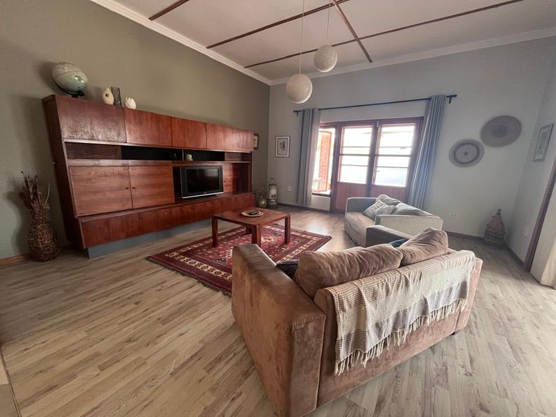 Spacious living room featuring laminate flooring, timber ceiling beams, and built-in wooden cabinetry with direct access to the outdoor area through french doors.