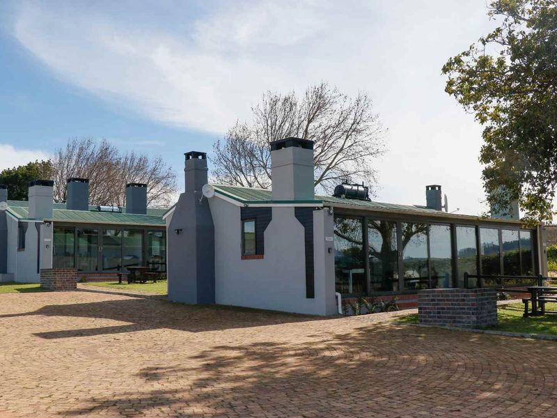 Exterior view of a cottage featuring a brick paved driveway, large glass sliding doors, and multiple masonry chimneys under a corrugated metal roof.
