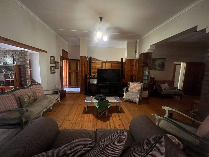 Spacious living room featuring warm timber flooring, traditional wood wall paneling, and an exposed brick feature pillar, offering a classic, rustic aesthetic.