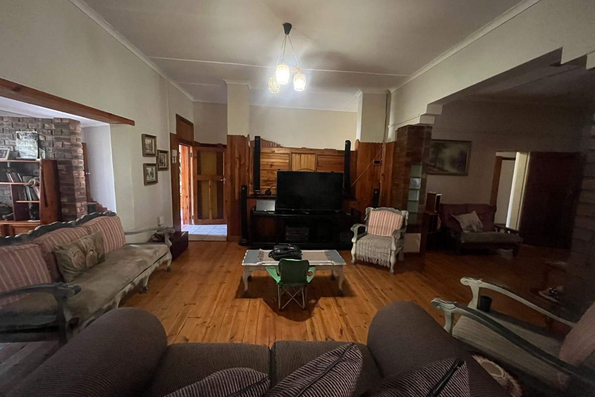 Spacious living room featuring warm timber flooring, traditional wood wall paneling, and an exposed brick feature pillar, offering a classic, rustic aesthetic.
