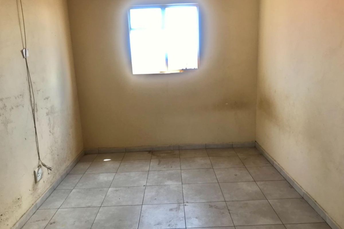 An empty bedroom featuring tiled flooring and a single window, requiring cosmetic updates and wall repairs.