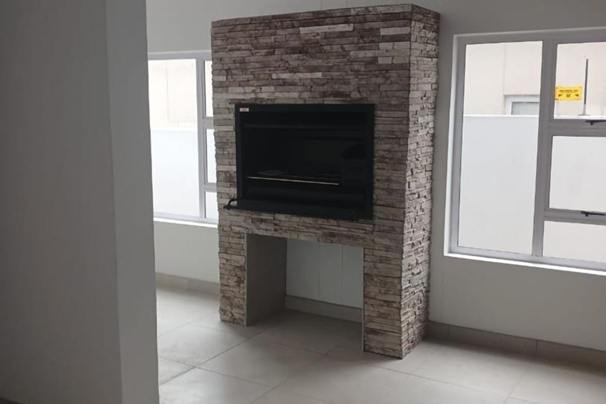 Spacious living area featuring a prominent stone-clad built-in fireplace, neutral tiled flooring, and large windows providing ample natural light.