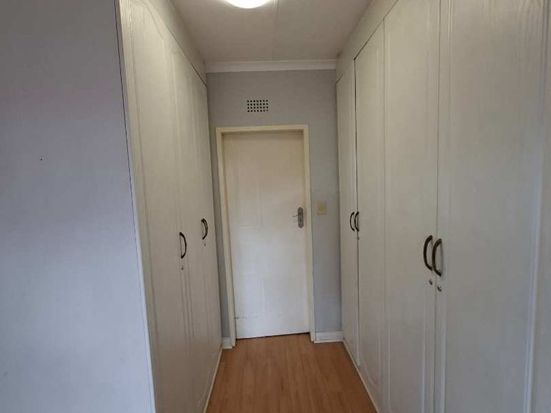 A functional hallway featuring extensive built-in storage cupboards and light-toned laminate flooring, providing a clean and organized transition space.