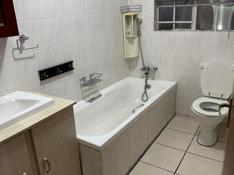 A functional bathroom featuring a bathtub, toilet, and vanity basin with tiled finishes throughout.