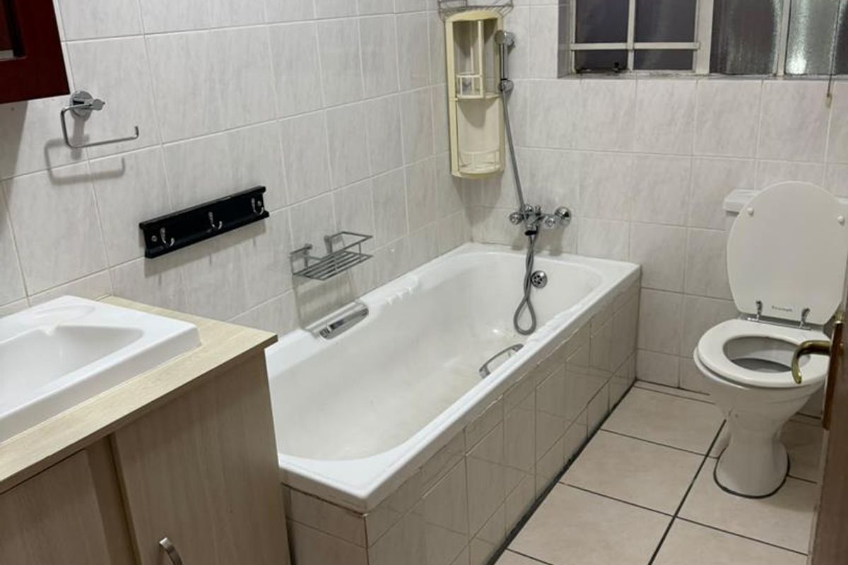 A functional bathroom featuring a bathtub, toilet, and vanity basin with tiled finishes throughout.