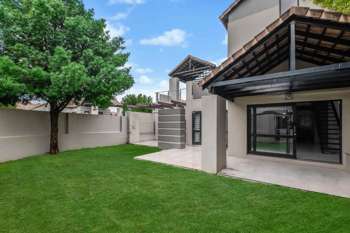 Rear view of the townhouse featuring a covered tiled patio, sliding glass doors, and a well-maintained private garden with perimeter walling.
