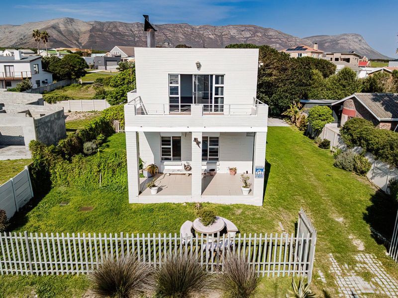 Aerial view of the rear elevation featuring a covered ground floor patio, an upper-level balcony, and a spacious garden with perimeter fencing.