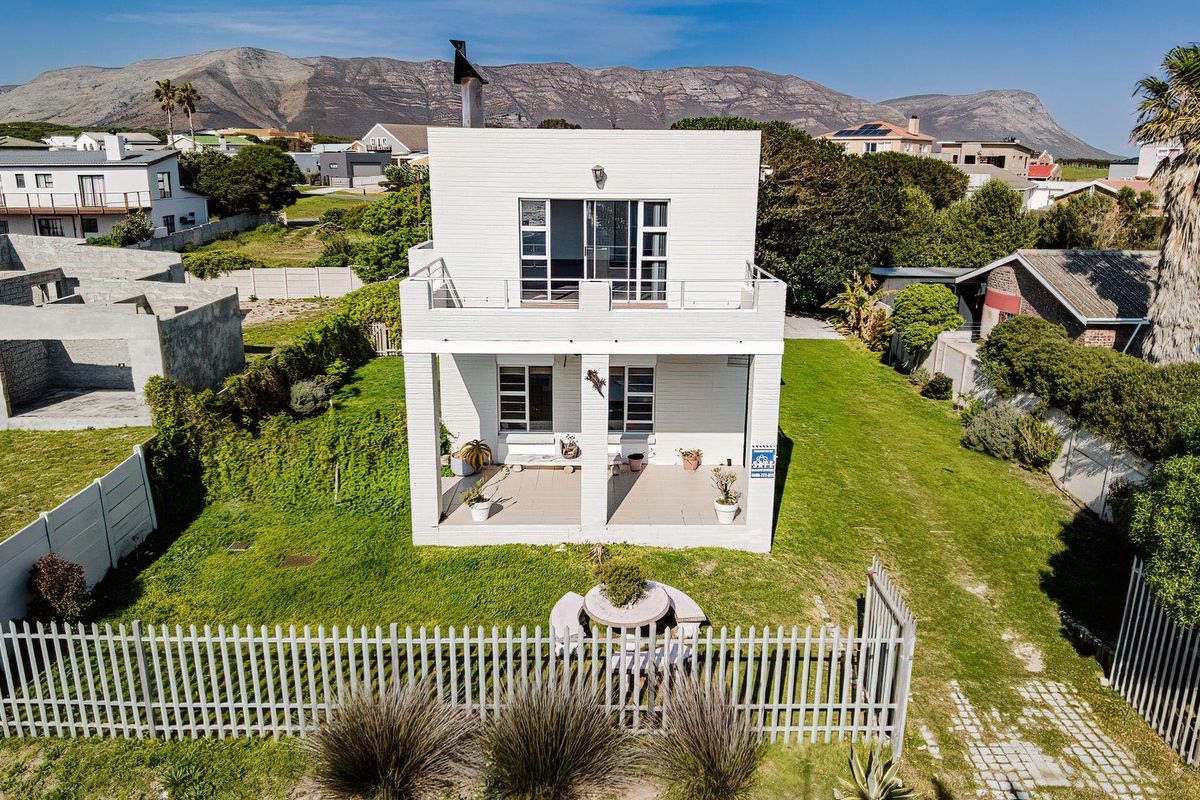 Aerial view of the rear elevation featuring a covered ground floor patio, an upper-level balcony, and a spacious garden with perimeter fencing.